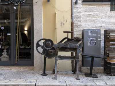 Dopo pochi passi, sulla destra, ci imbattiamo invece in un antico macchinario poggiato sul marciapiede. Si tratta di una piegatrice per carta degli anni 30 situata un tempo all�interno della filiale di una banca attiva in questo punto fino agli anni 80